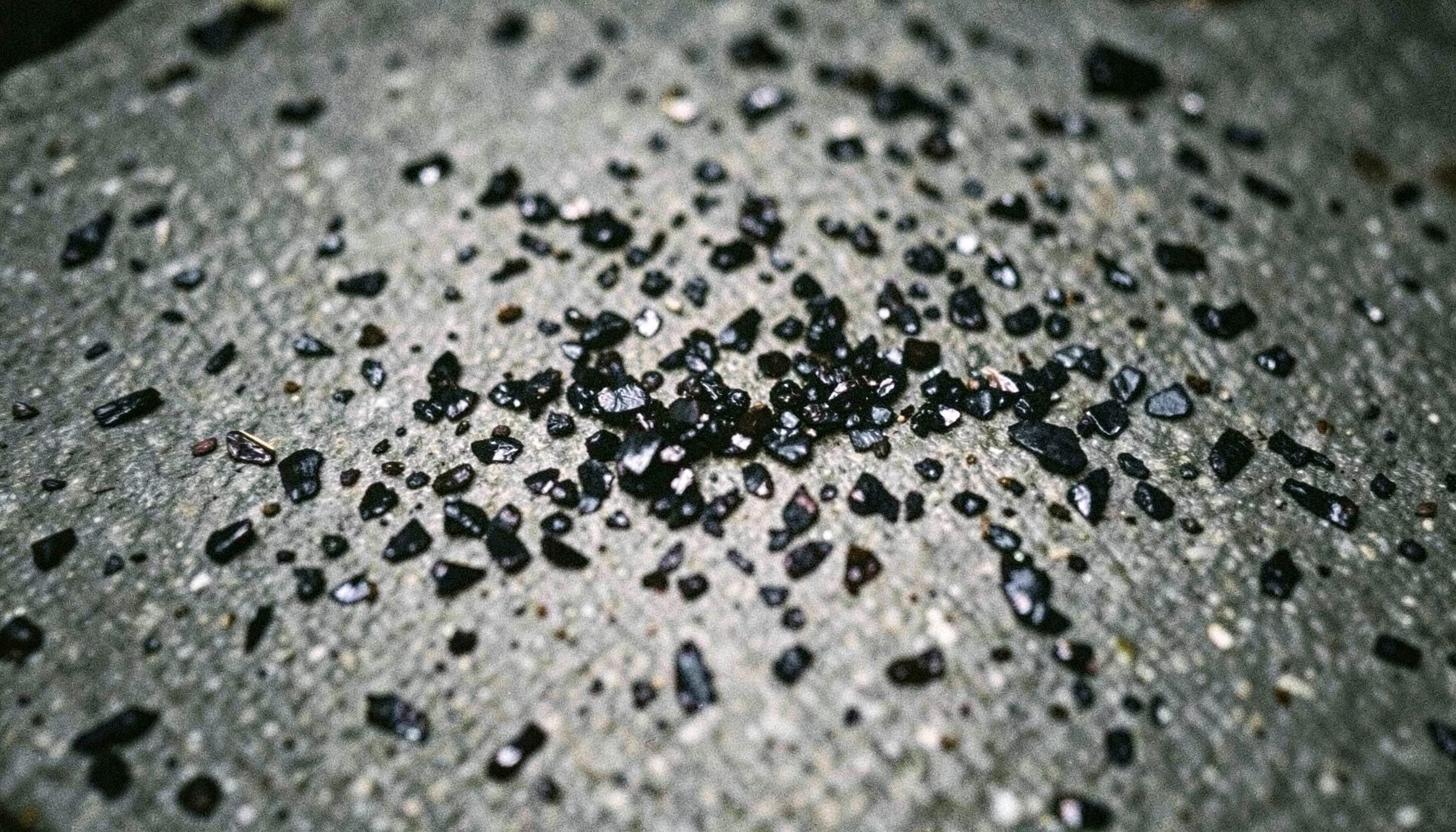 Dark, shimmering mineral flakes scattered across a textured gray stone surface, moody and natural